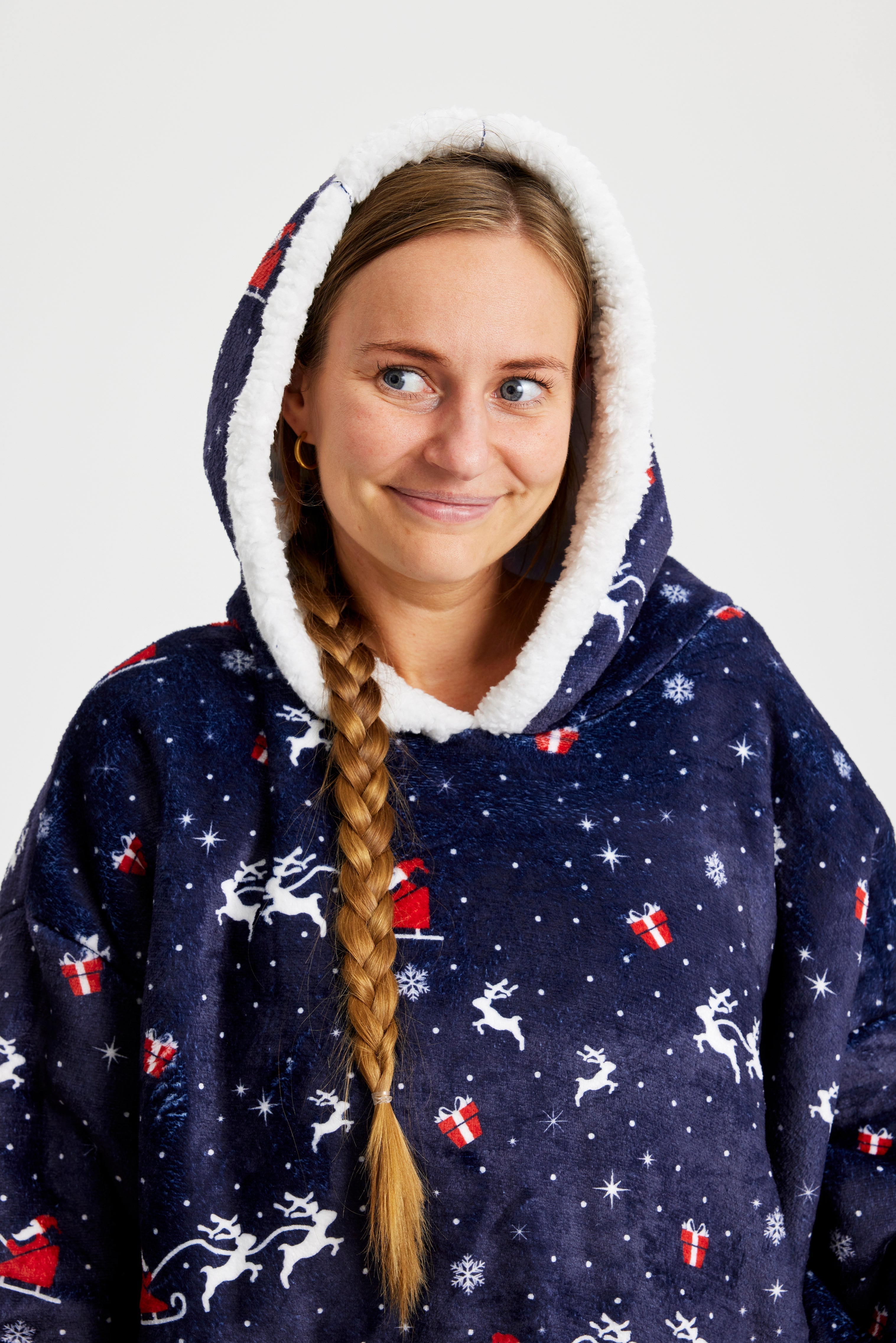 Eine Frau mit langem Zopf, die einen blauen gemusterten Weihnachts-Kapuzenpullover trägt.